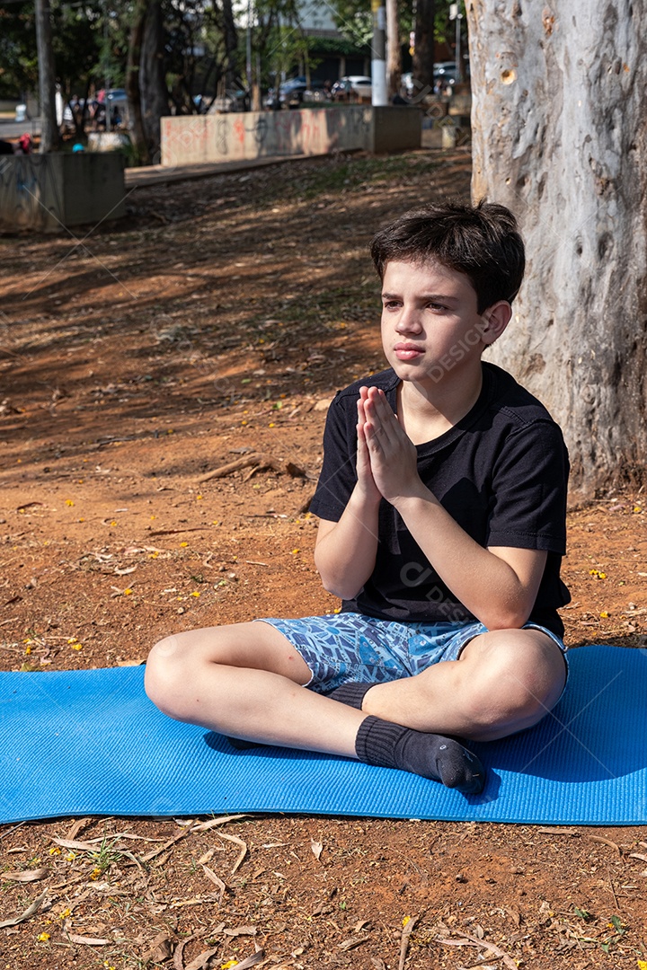 Menino sentado no tapete de yoga se alongando na aula ao ar livre