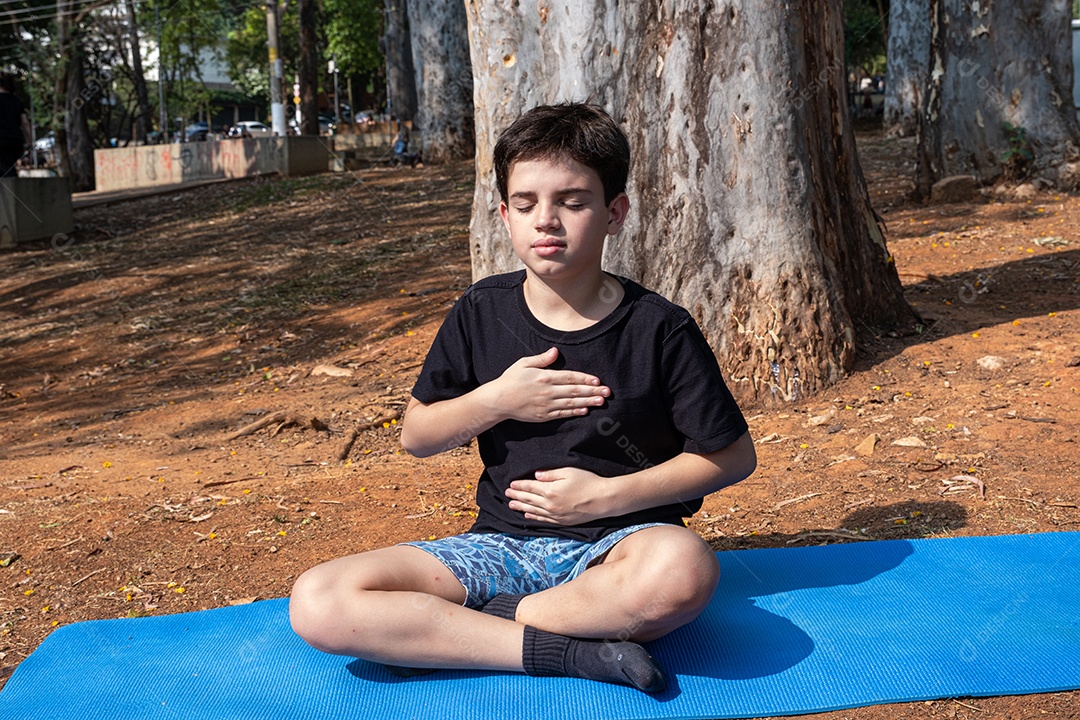 Menino sentado no tapete de yoga se alongando na aula ao ar livre