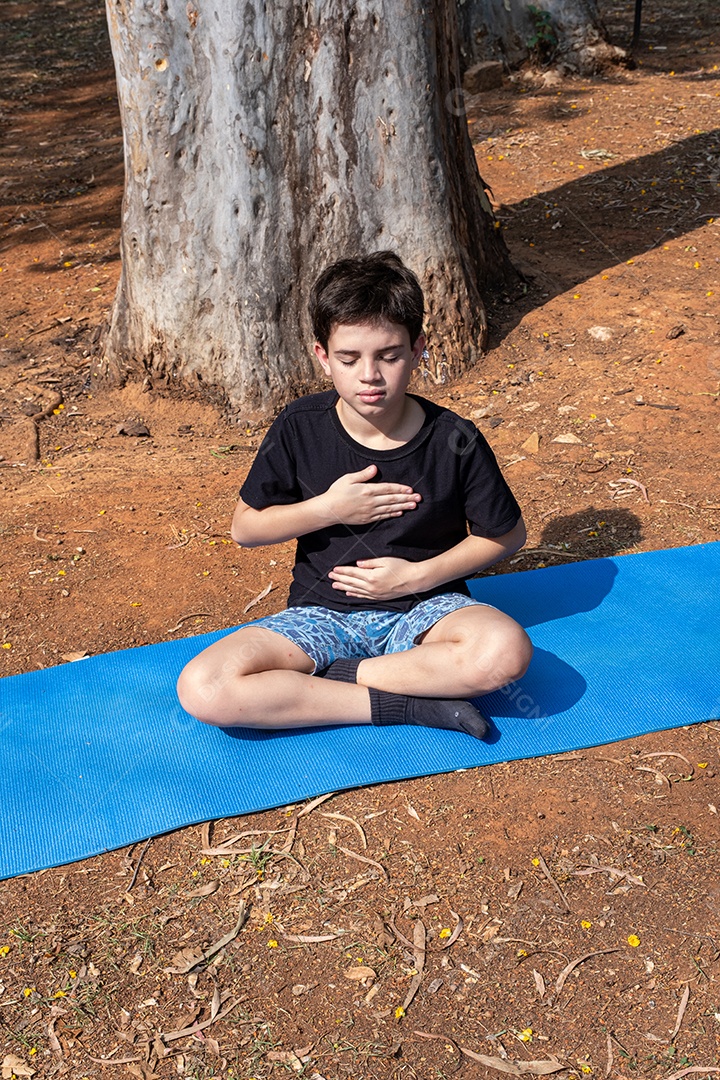 Criança sentada no tapete de yoga e se alongando na aula ao ar livre