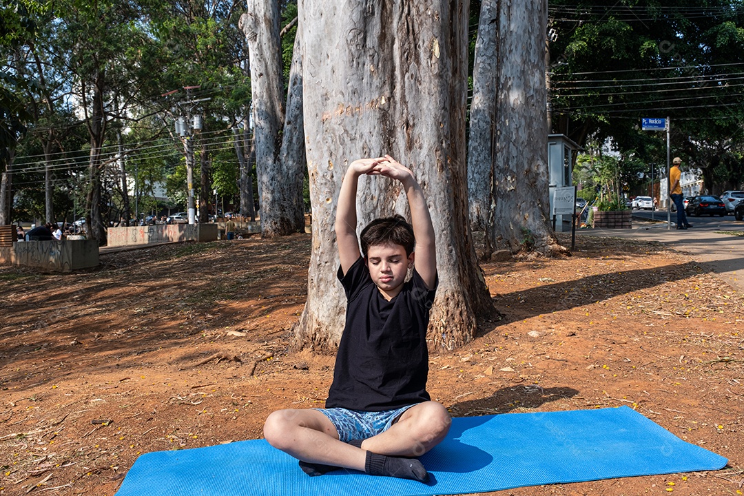 Criança sentada no tapete de yoga e se alongando na aula ao ar livre