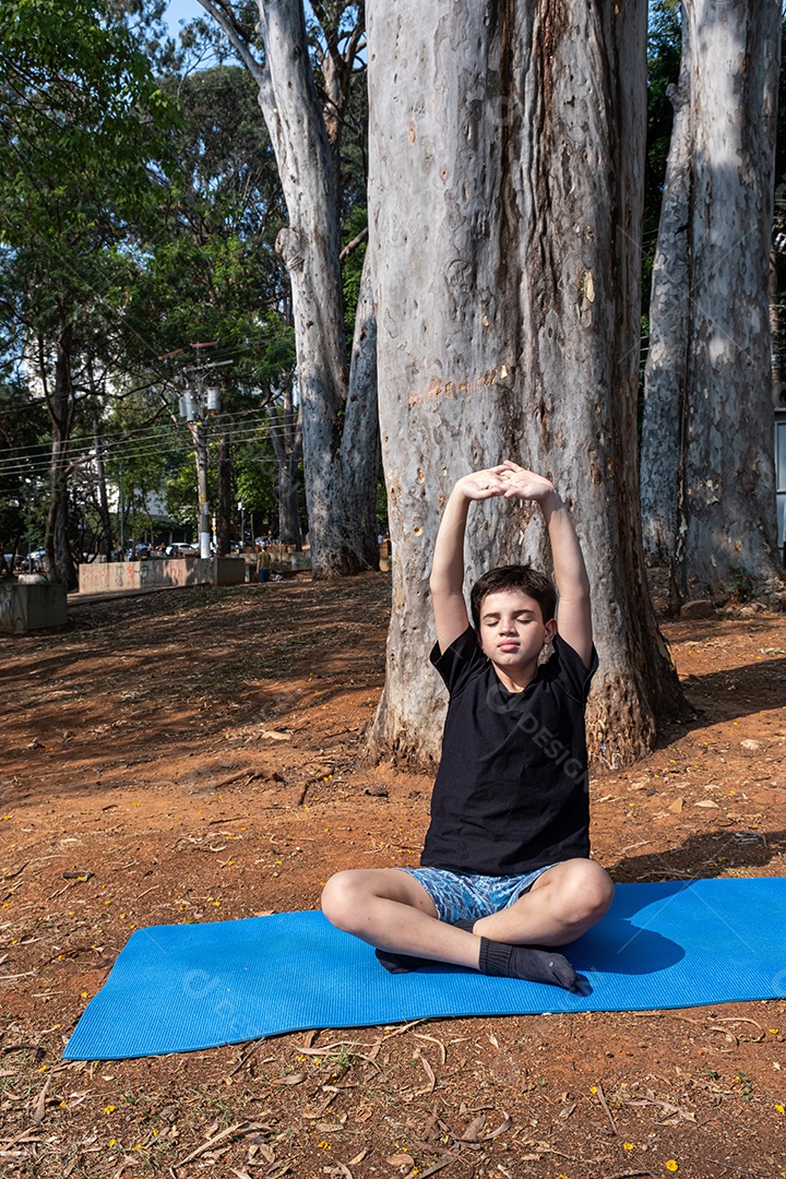 Criança sentada no tapete de yoga e se alongando na aula ao ar livre