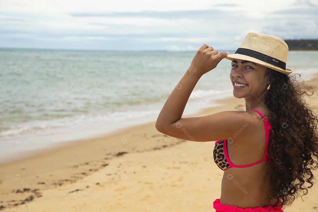 Linda jovem com mão no chapéu em uma praia