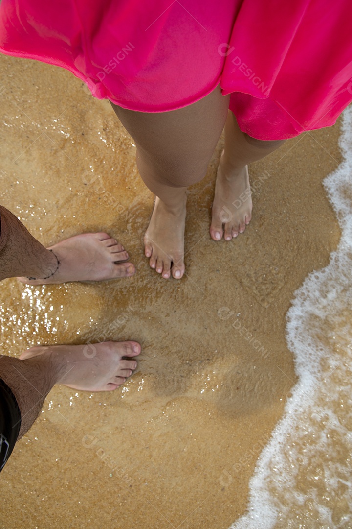 Um casal com pés na areia de uma praia