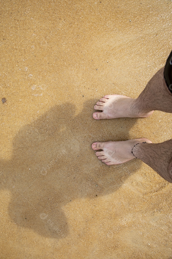 Homem com pés na areia de uma praia