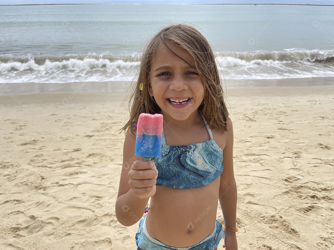 Menina feliz na praia com seu picolé colorido