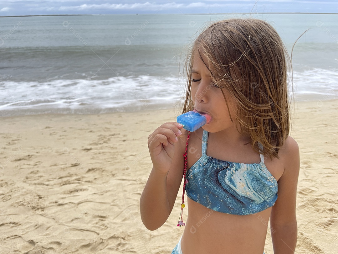 Menina linda com picolé na mão se divertindo na praia