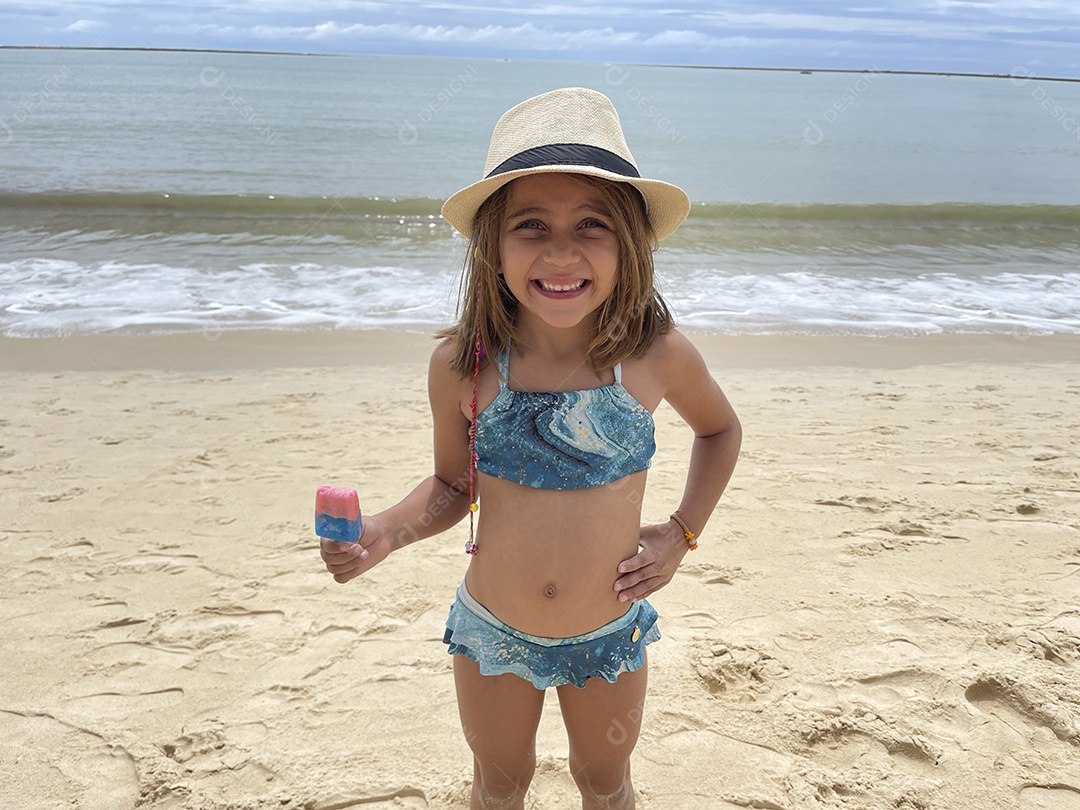 Uma linda menininha com picolé na mão em uma praia