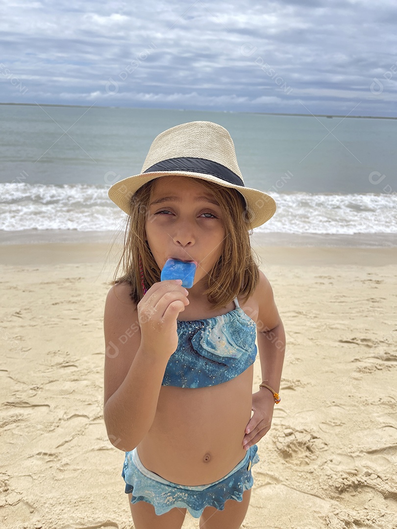 Garotinha se divertindo na praia tomando um delicioso picolé
