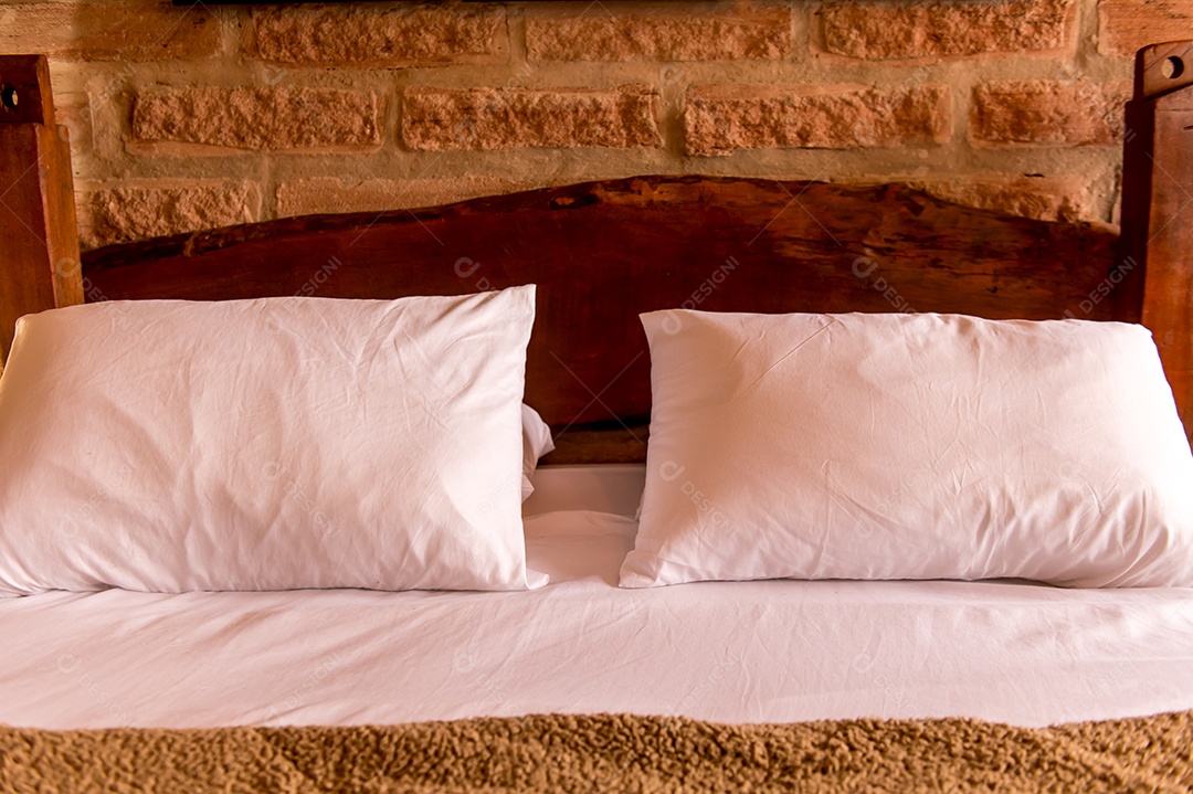 Cama com travesseiros brancos e cabeceira de madeira