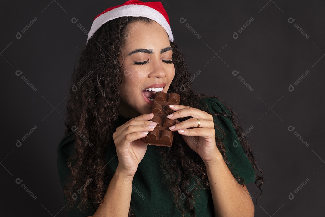 Mulher com gorro vermelho e mordendo barra de chocolate