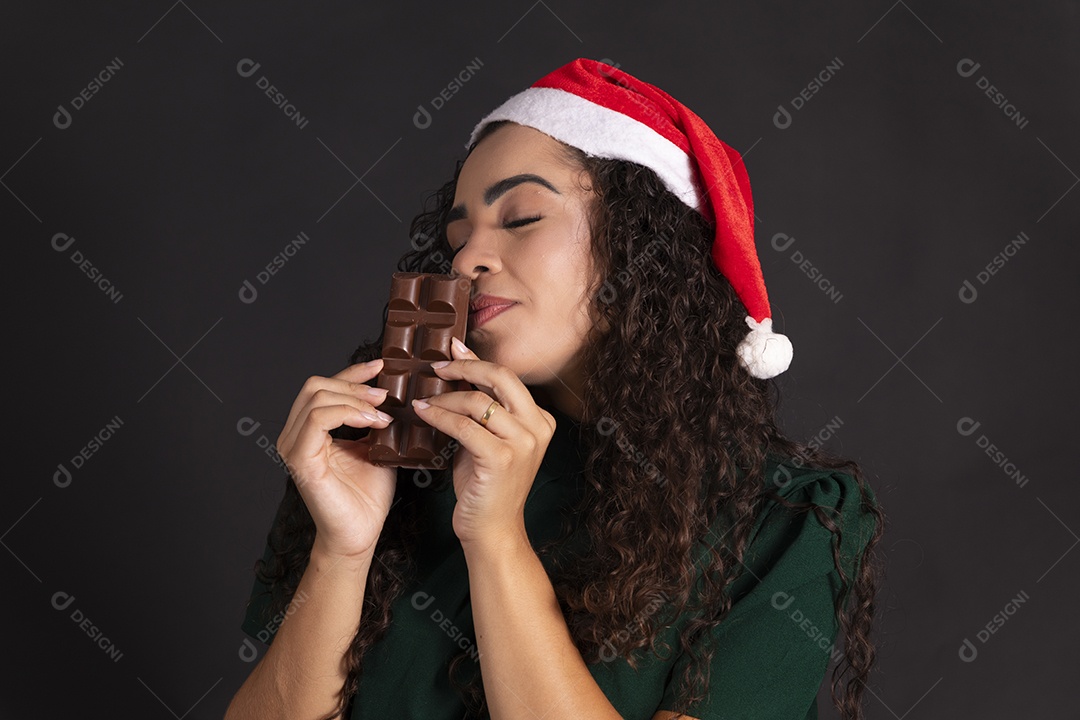 Mulher com gorro de papai noel e barra de chocolate na mão