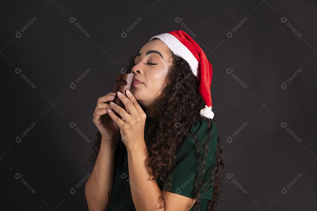Mulher com gorro de natal e segurando barra de chocolate na mão