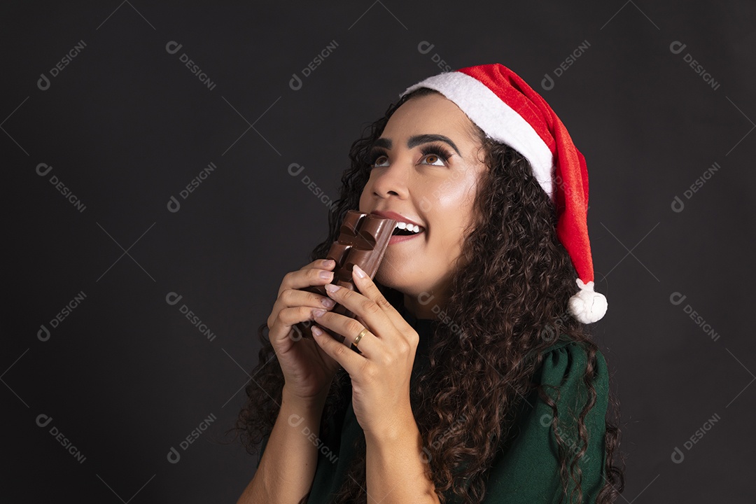 Mulher com gorro de natal e segurando barra de chocolate na mão