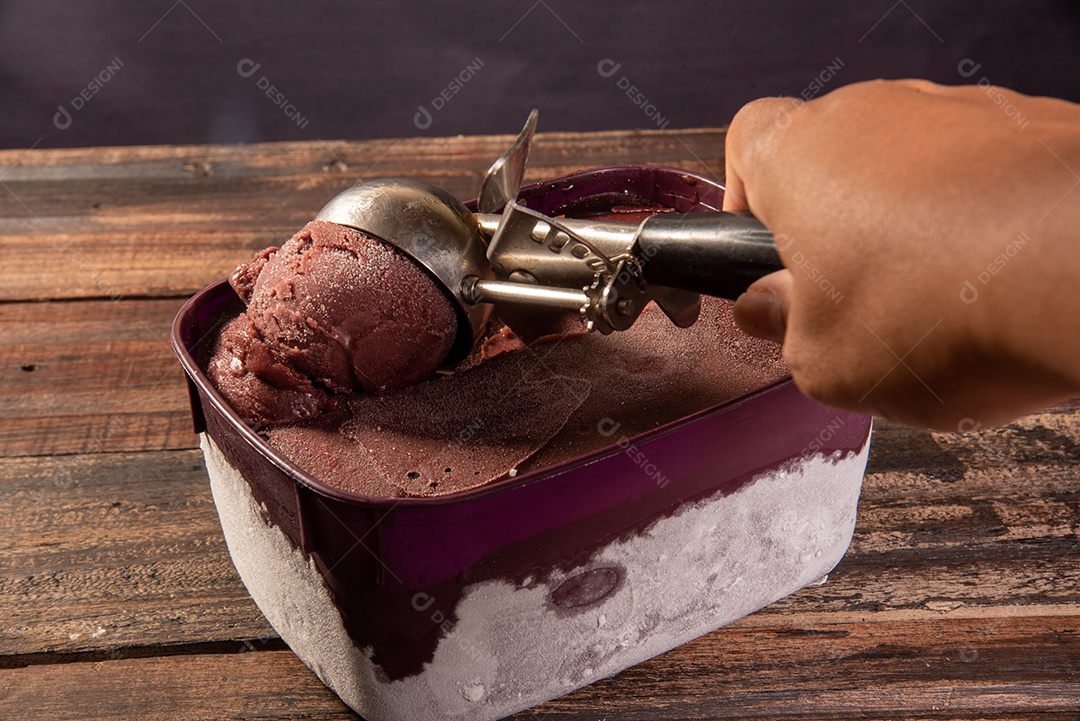Mão tirando açaí brasileiro congelado do pote de sorvete