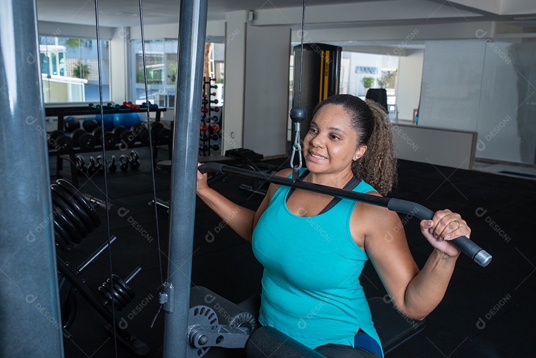Mulher desportiva exercitando em multiestação na academia