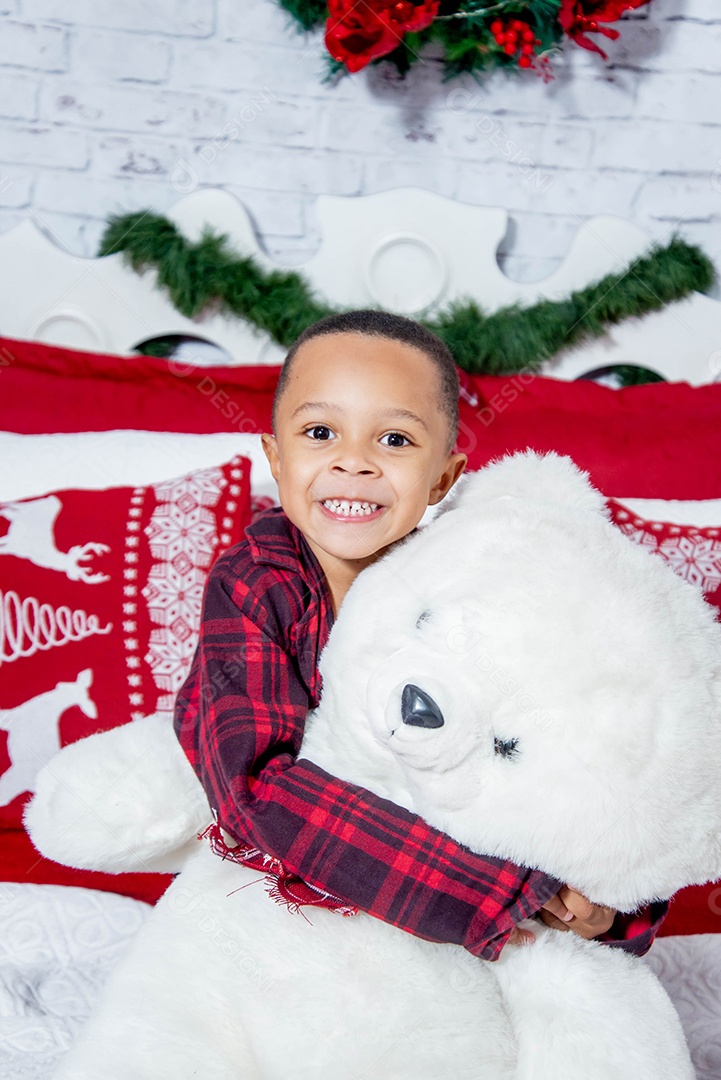 Um lindo menino abraçado com urso de pelúcia feliz em decoração natalina
