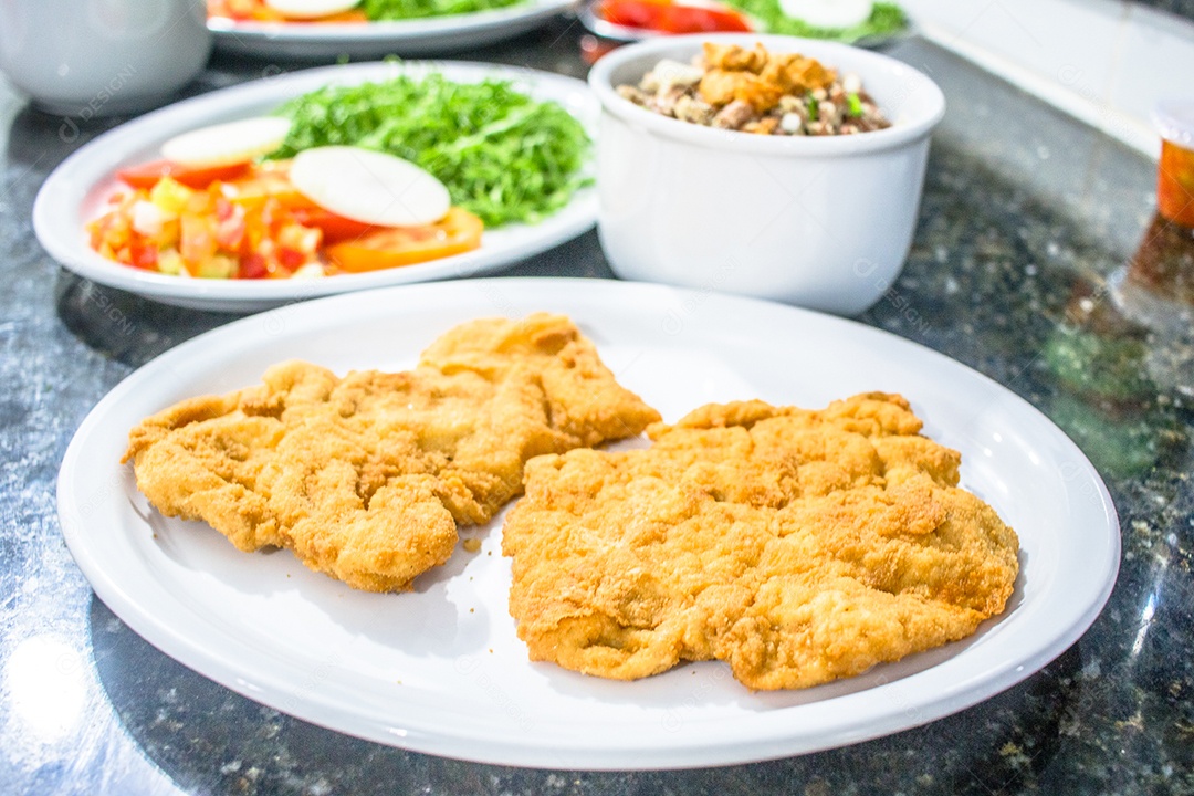 Bife à milanesa de forno com acompanhamentos sobre mesa de pedra