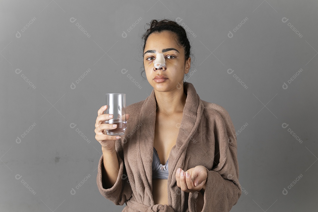 Mulher com segurando um copo de água e nariz enfaixado