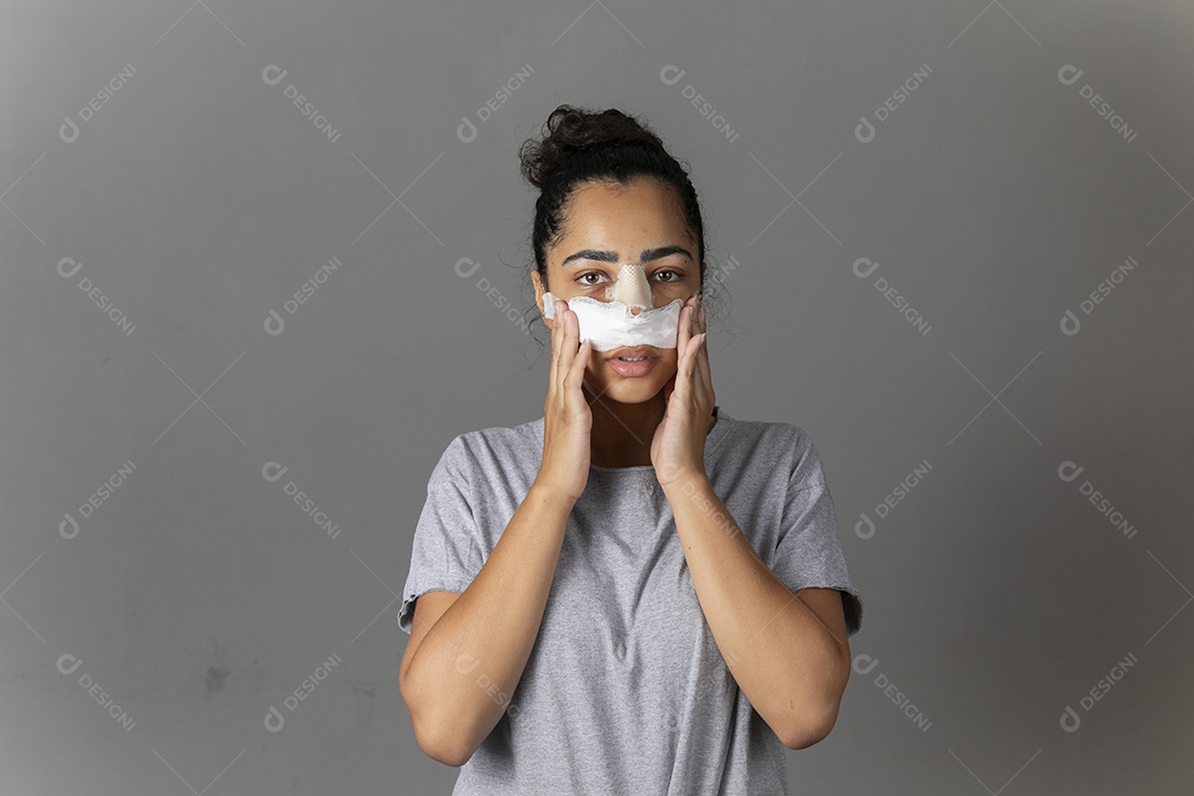 Mulher com curativo no nariz e mãos no rosto