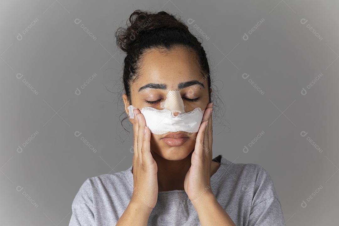 Mulher com curativo no nariz e mãos no rosto