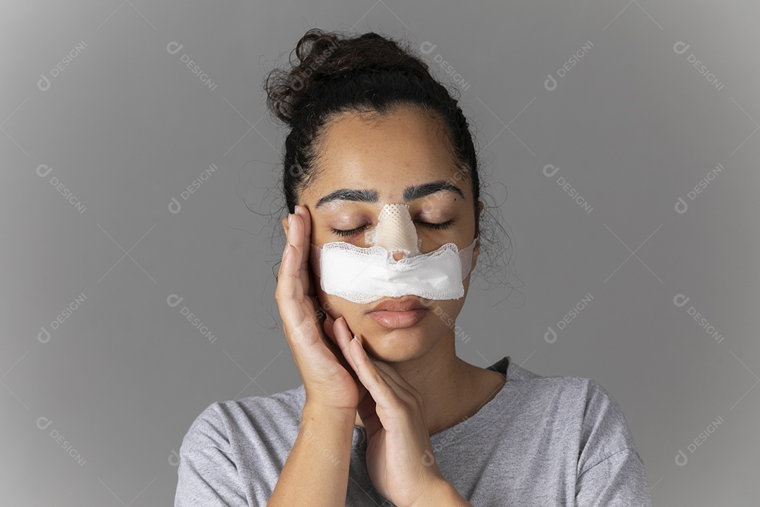 Mulher com curativo no nariz e mãos no rosto