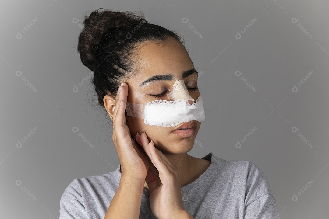 Mulher com curativo no nariz e mão no rosto