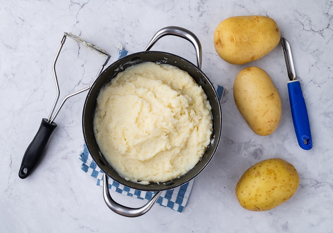 Purê de batatas em uma panela com batatas e utensílios
