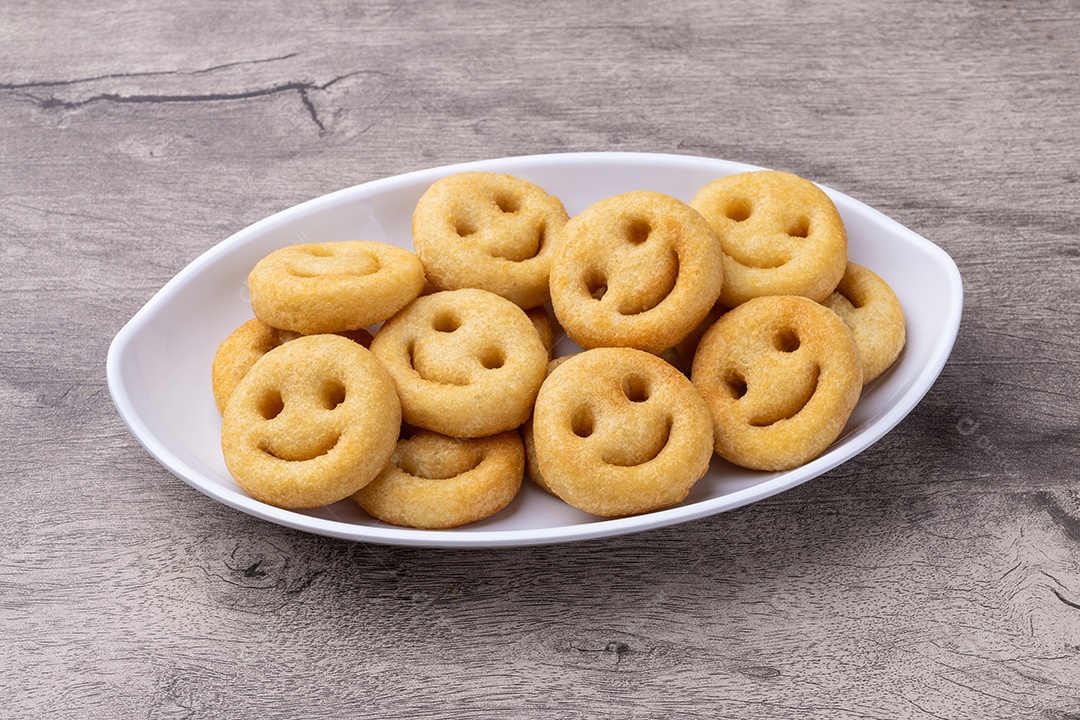 Batatas fritas sorridentes em um prato sobre a mesa de madeira