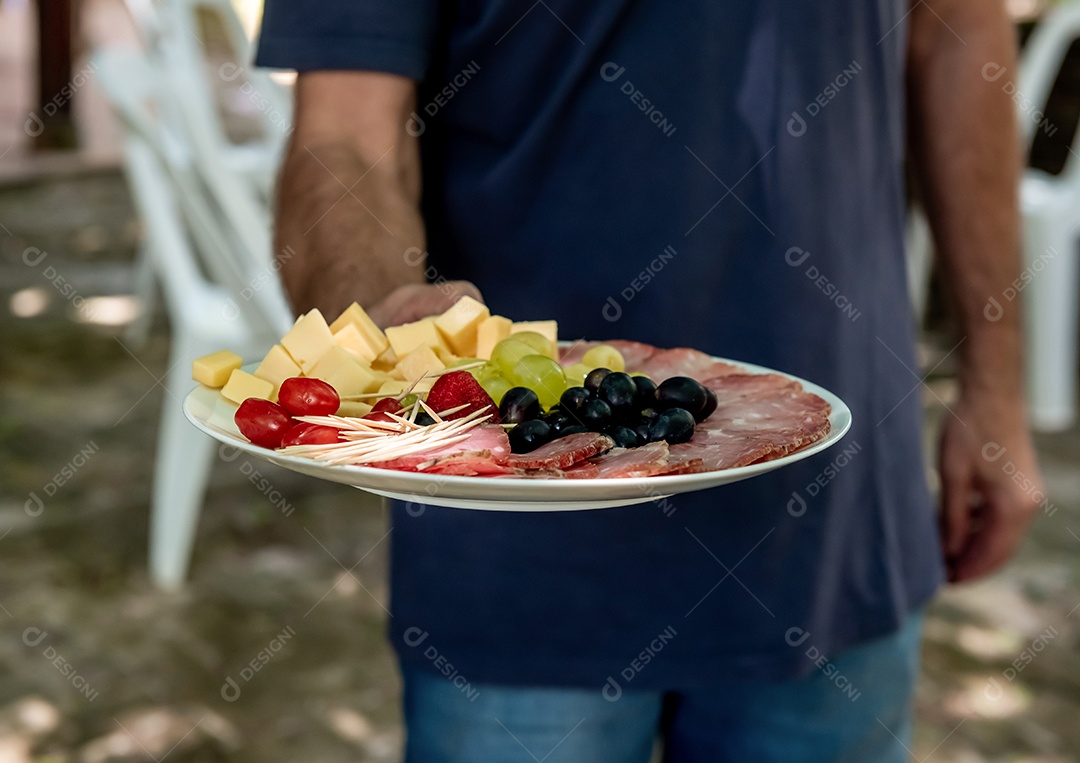 Garçom servindo aperitivos de festa queijo salame e frutas vermelhas