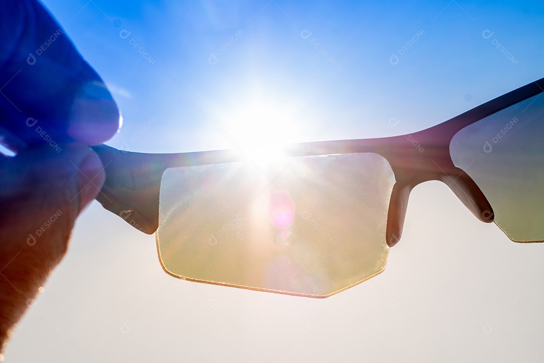 Close up Mão segurando óculos de sol esportivos elegantes contra o céu brilhante e o fundo do sol