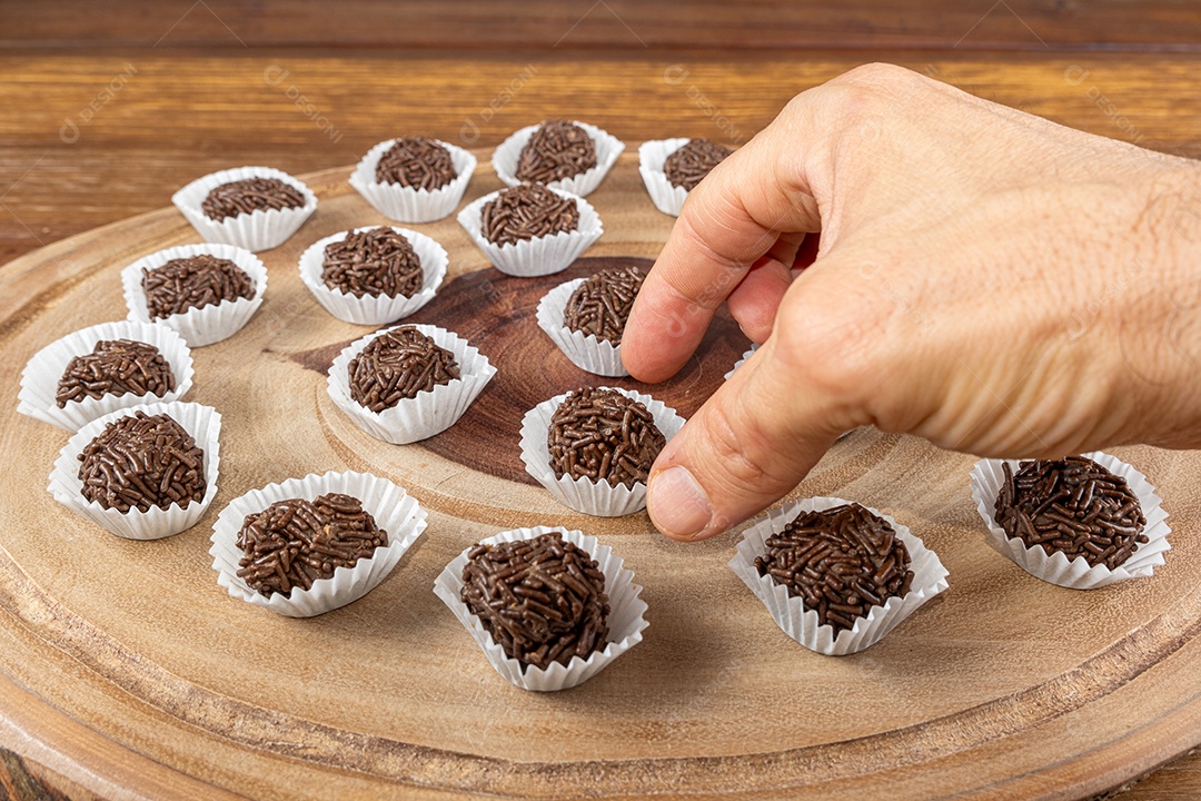 Mão pegando brigadeiro de chocolate sobre uma tábua de madeira