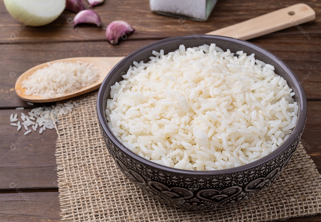 Arroz branco cozido em uma tigela sobre a mesa de madeira com cebola louro e alho