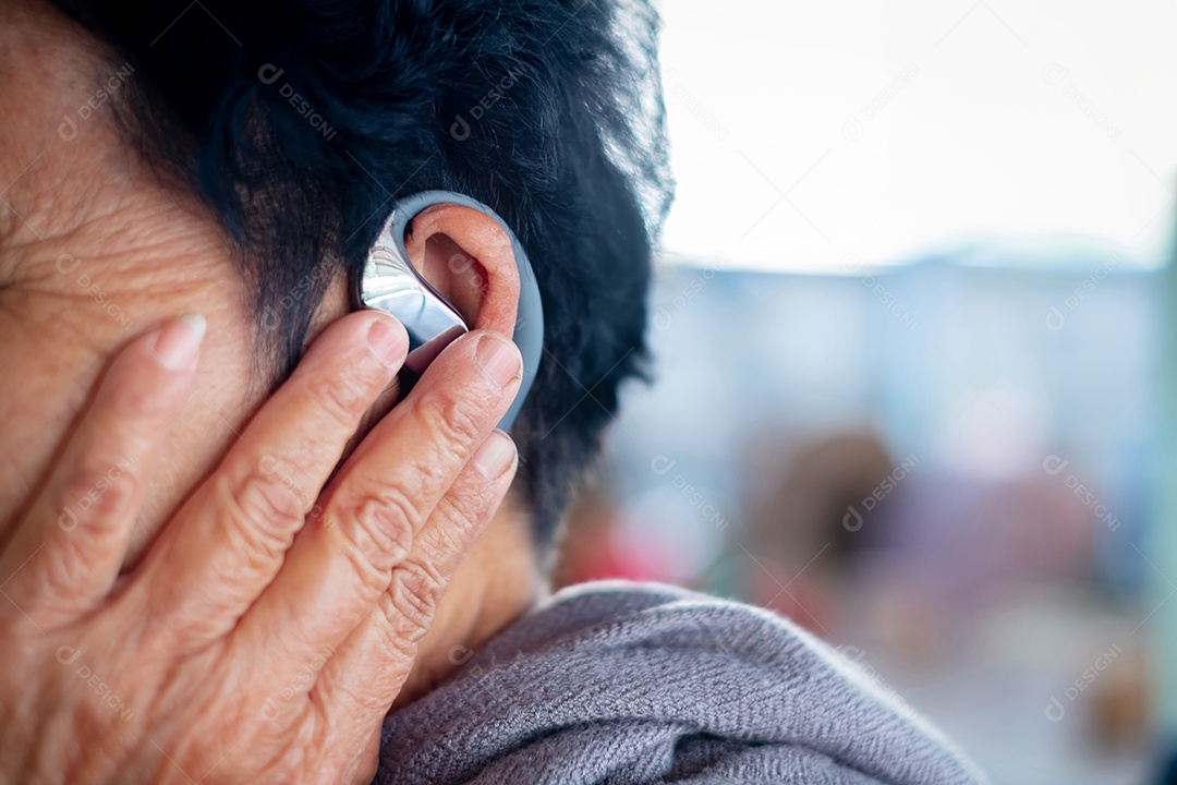 Mão de mulher idosa toca aparelho auditivo