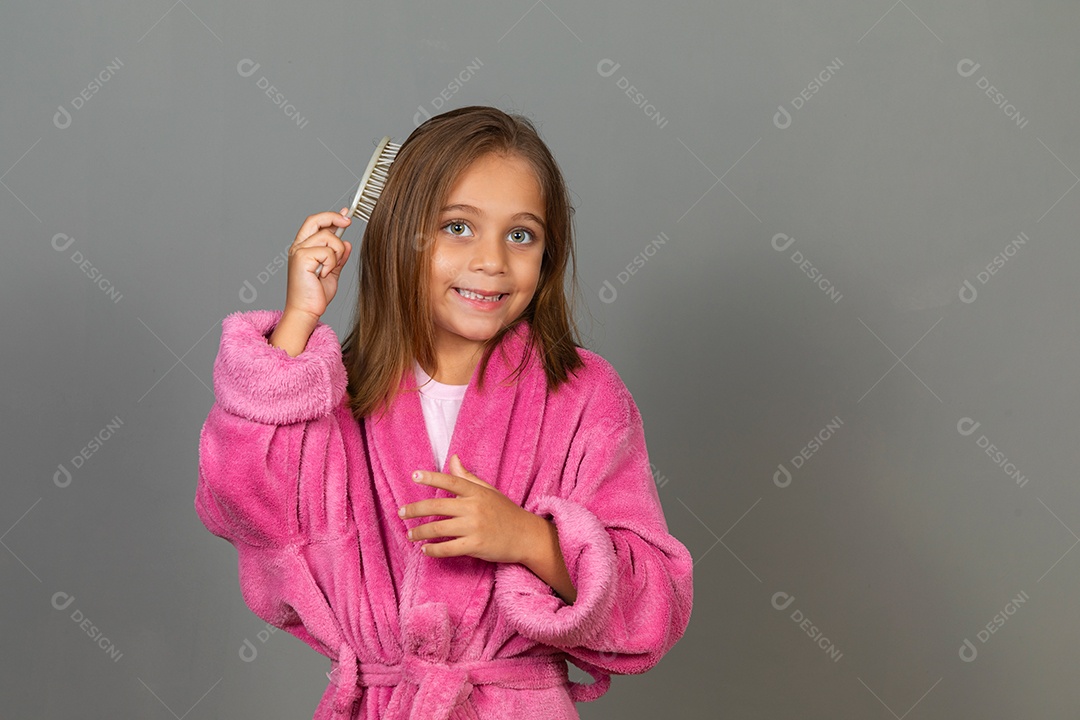 Linda menina usando roupão de banho sobre fundo rosa do isolado segurando escova de cabelo