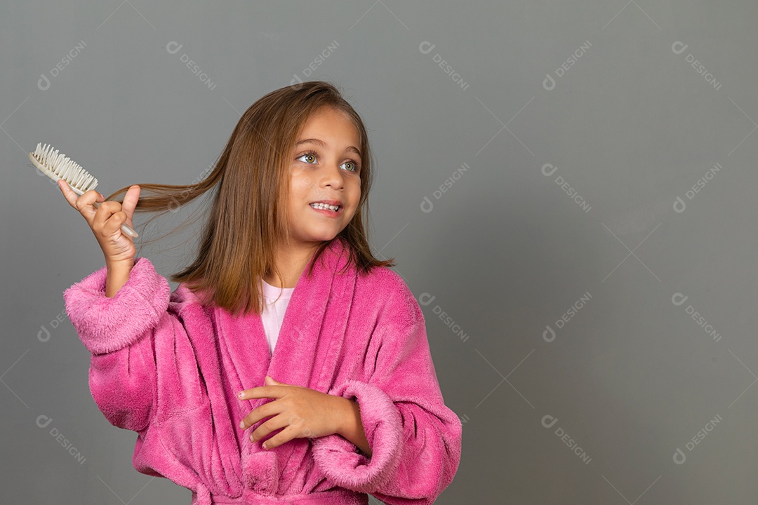 Linda menina usando roupão de banho sobre fundo rosa do isolado penteando o cabelo