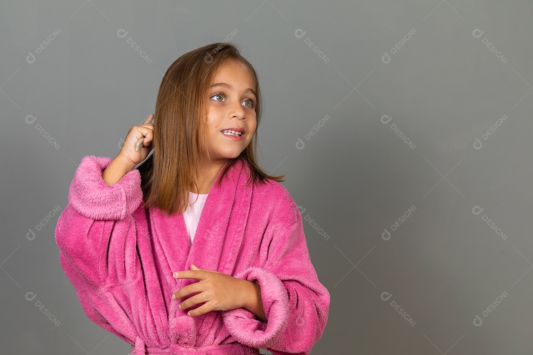 Linda menina usando roupão de banho sobre fundo rosa do isolado penteando o cabelo