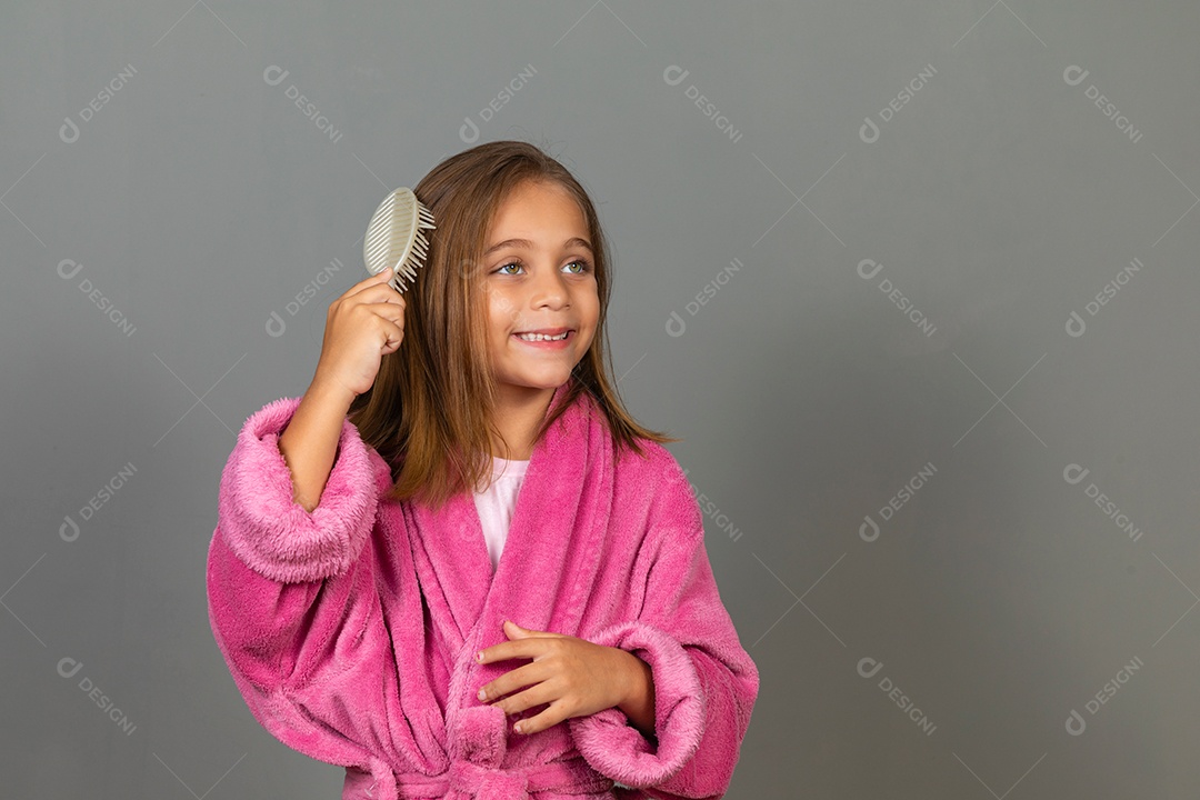 Linda menina usando roupão de banho sobre fundo rosa do isolado penteando o cabelo