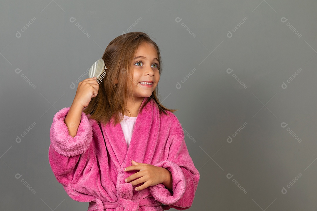 Linda menina usando roupão de banho sobre fundo rosa do isolado penteando o cabelo