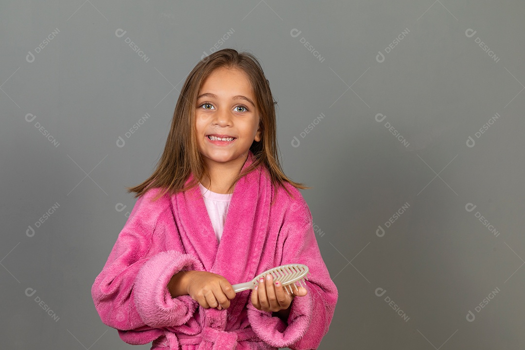 Linda menina usando roupão de banho sobre fundo rosa do isolado segurando escova de cabelo