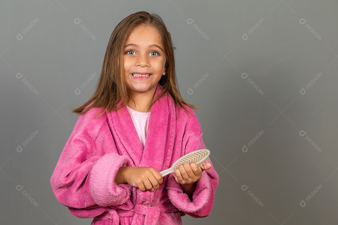 Linda menina usando roupão de banho sobre fundo rosa do isolado segurando escova de cabelo