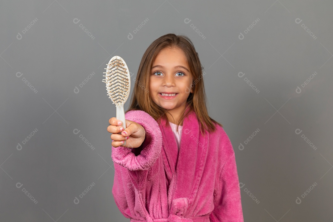 Linda menina usando roupão de banho sobre fundo rosa do isolado segurando escova de cabelo