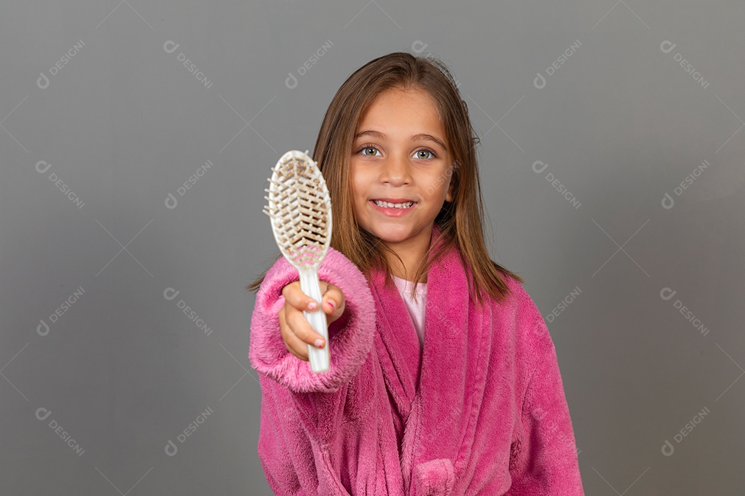 Linda menina usando roupão de banho rosa sobre fundo isolado segurando escova de cabelo