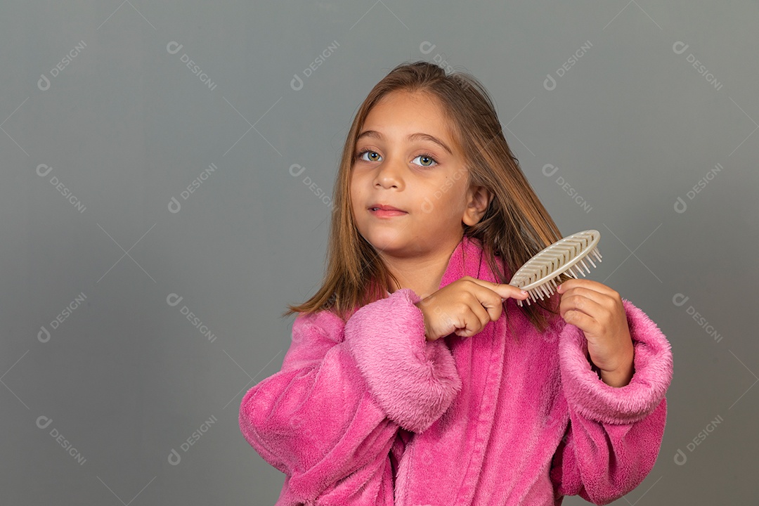 Linda menina usando roupão de banho sobre fundo rosa do isolado escovando o cabelo