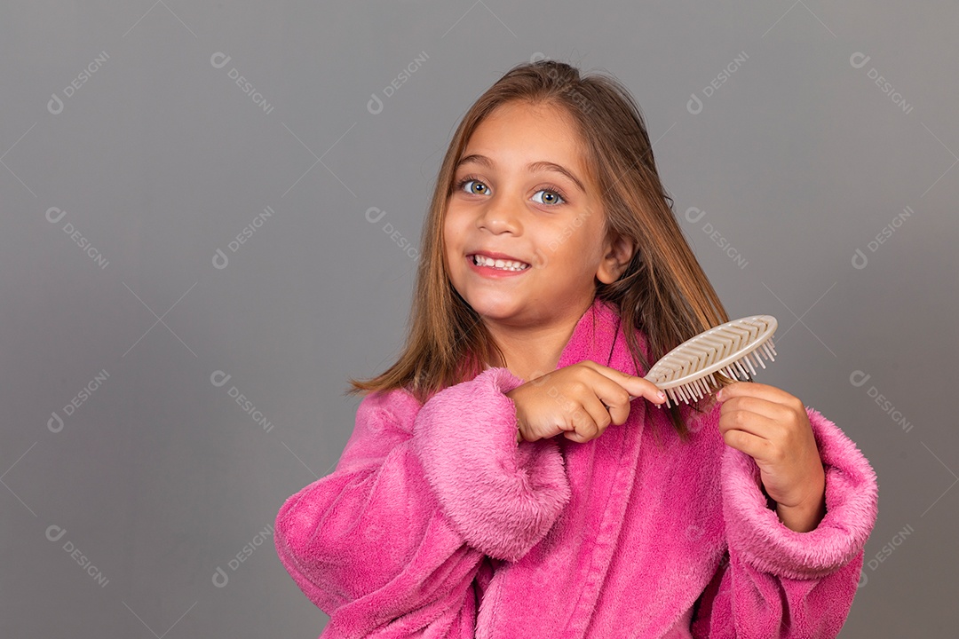 Linda menina usando roupão de banho sobre fundo rosa do isolado peteando o cabelo