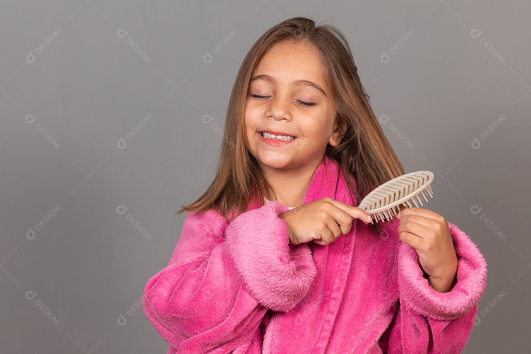 Linda menina usando roupão de banho sobre fundo rosa do isolado escovando o cabelo
