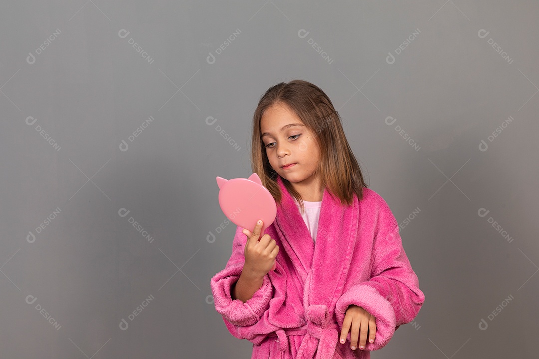 Linda menina usando roupão de banho rosa sobre fundo isolado segurando espelho