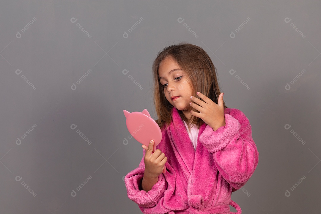 Linda menina usando roupão de banho rosa sobre fundo isolado segurando espelho