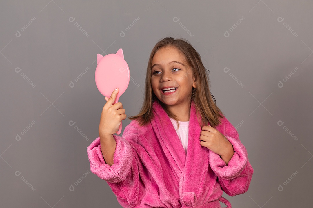 Linda menina usando roupão de banho rosa sobre fundo isolado segurando espelho