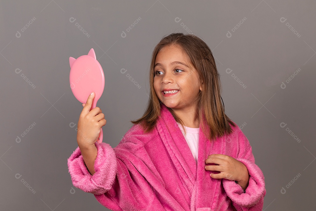Linda menina usando roupão de banho rosa sobre fundo isolado segurando espelho