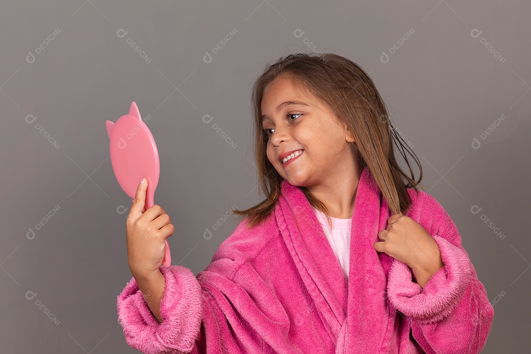 Linda menina usando roupão de banho rosa sobre fundo isolado segurando espelho